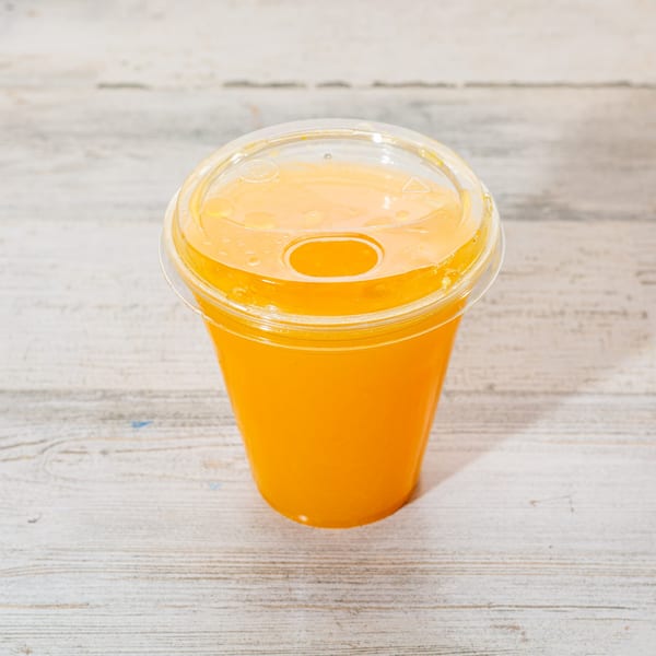 Fresh orange juice in a clear plastic cup with a lid, on a light wooden surface.