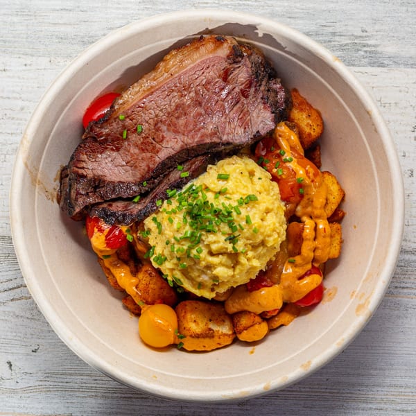 EGGDOSE breakfast bowl with steak, scrambled eggs, potatoes, tomatoes, and sauce.