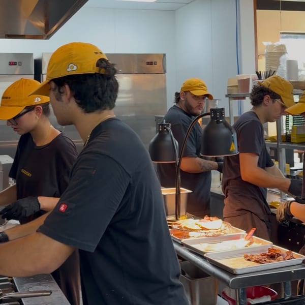 Restaurant kitchen with several staff in yellow caps preparing food under heat lamps.
