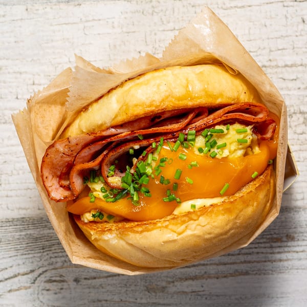 EGGDOSE breakfast sandwich with bacon, scrambled eggs, cheese, and chives in a paper wrapper.