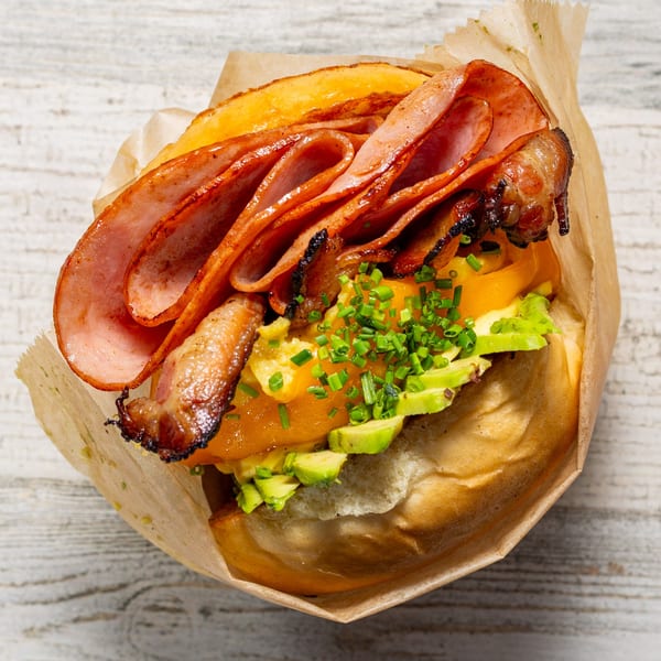 EGGDOSE breakfast sandwich with ham, bacon, scrambled eggs, avocado, and chives in a paper wrap.