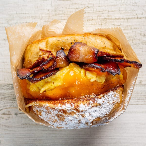 EGGDOSE breakfast sandwich with bacon, egg, and cheese on a brioche bun, dusted with powdered sugar.