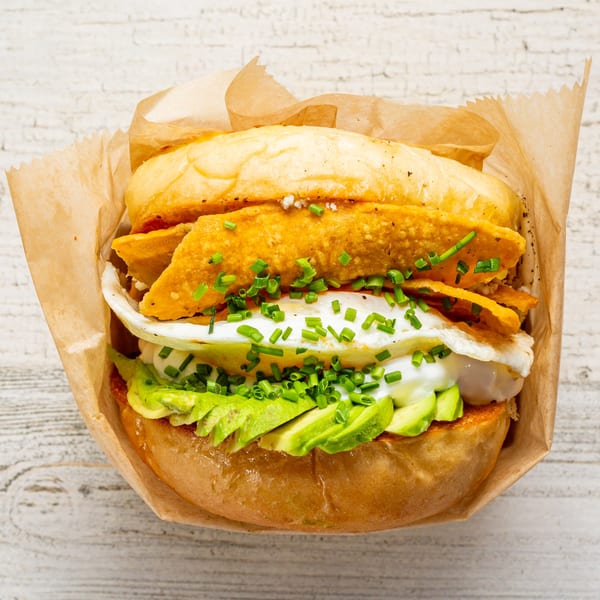 EGGDOSE breakfast sandwich with egg, avocado, chives, and tortilla strips in a paper wrapper.