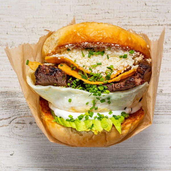 EGGDOSE breakfast sandwich with steak, fried egg, avocado, and cheese on a bun.